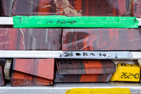 trays of rock core samples aligned and labeled, showing depth. The samples are striated in grays, oranges, deep oranges.