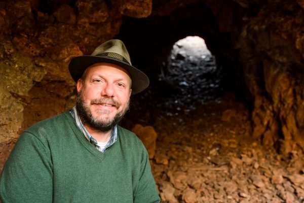 John Hawks poses in front of a cave.