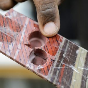 Closeup of rock samples from the Barberton core, with two holes drilled out of them, and a finger pointing to the striated colors