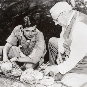 Historical black and white photo of John Robinson (student) and Robert Broom (teacher) at the mouth of a cave.
