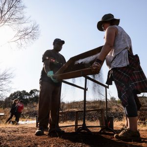University of the Witwatersrand field assistant Andrew Moyagabo Phaswana and UW-Madison student Emmaleigh Grady use a sifting screen to sort for potential artifacts.